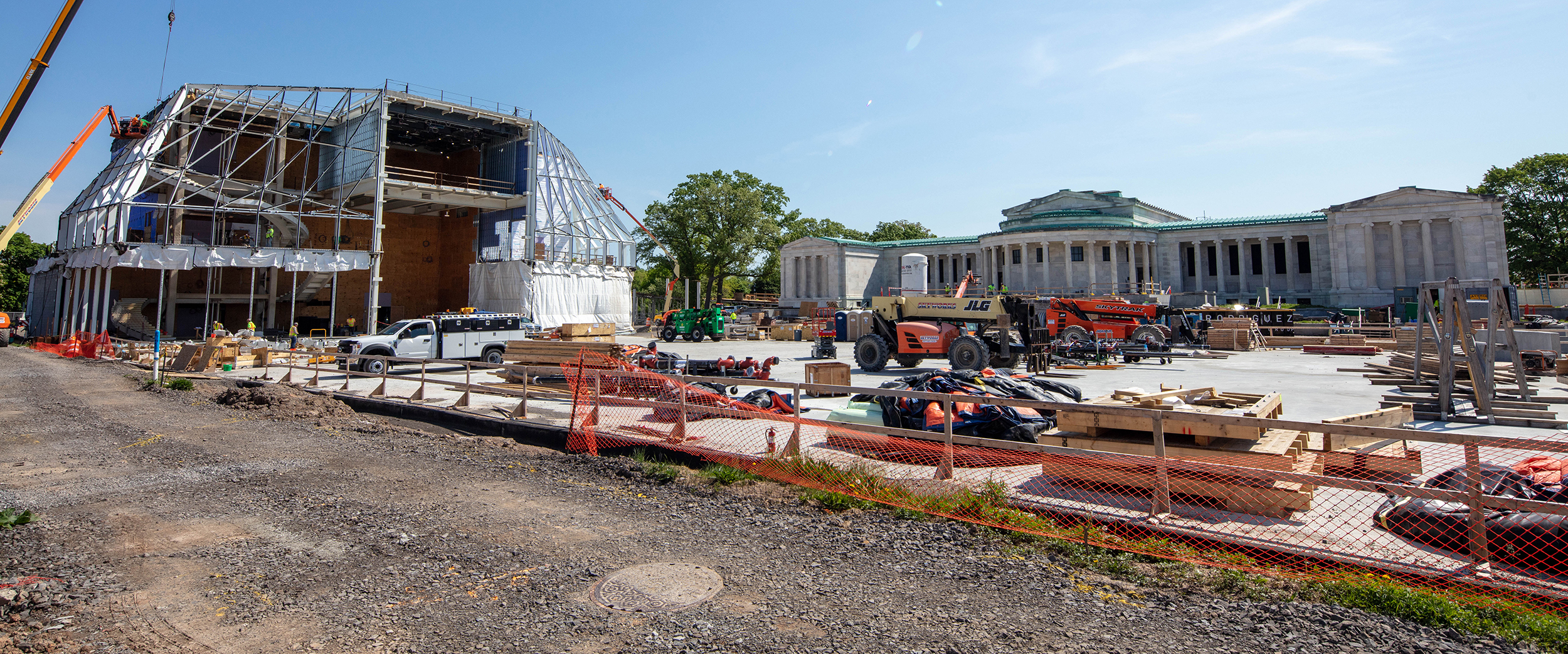 A construction site with the steel frame of a new building on the left and a white marble building with a green copper roof on the right