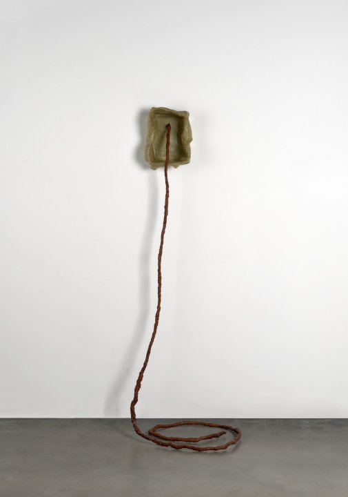 A beige fiberglass rectangle opening on a white wall with a red wire protruding from the center and reaching the cement floor.   