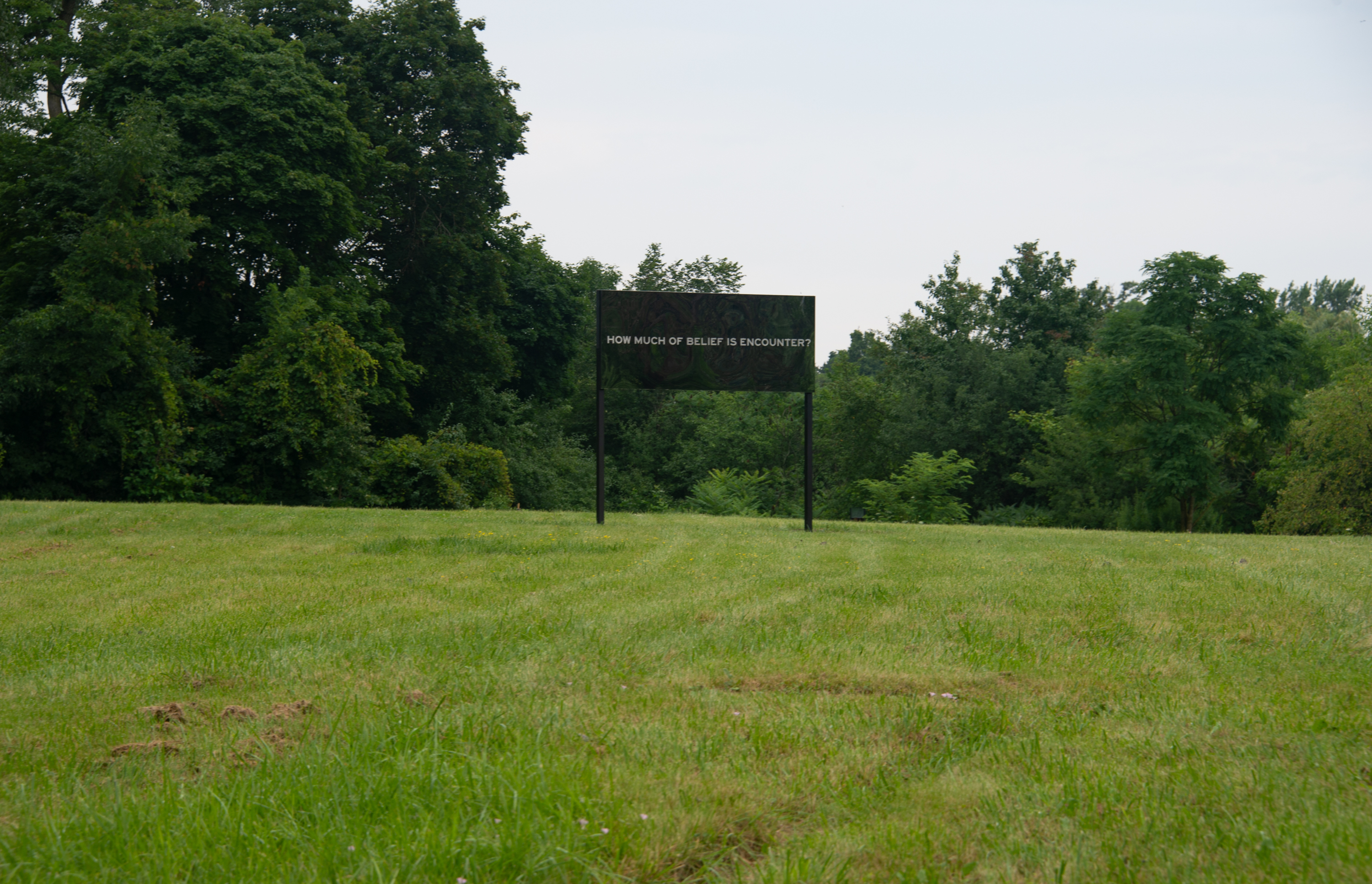 A mirrored billboard that reads "How much of belief is encounter?"