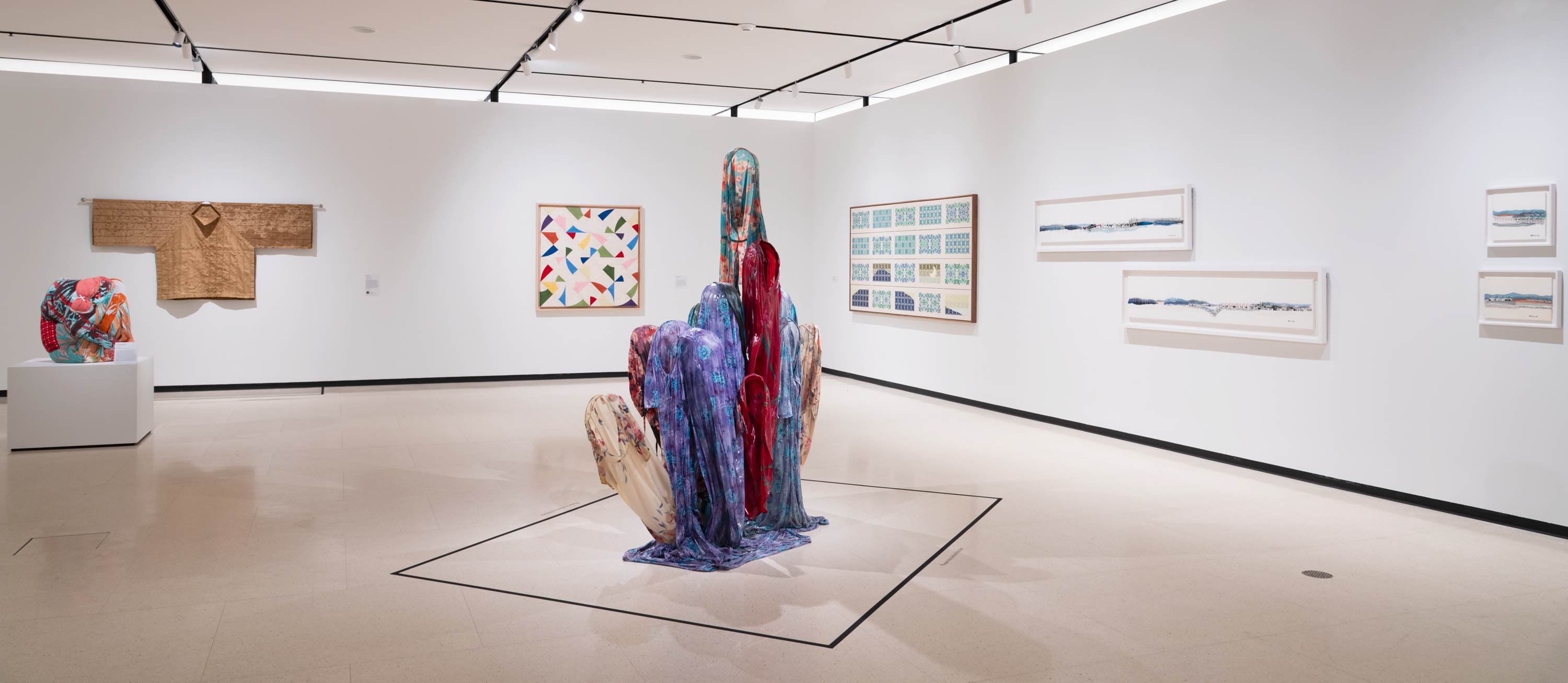 Installation view of an art gallery with works hanging on white walls and a colorful sculpture in the center of the room