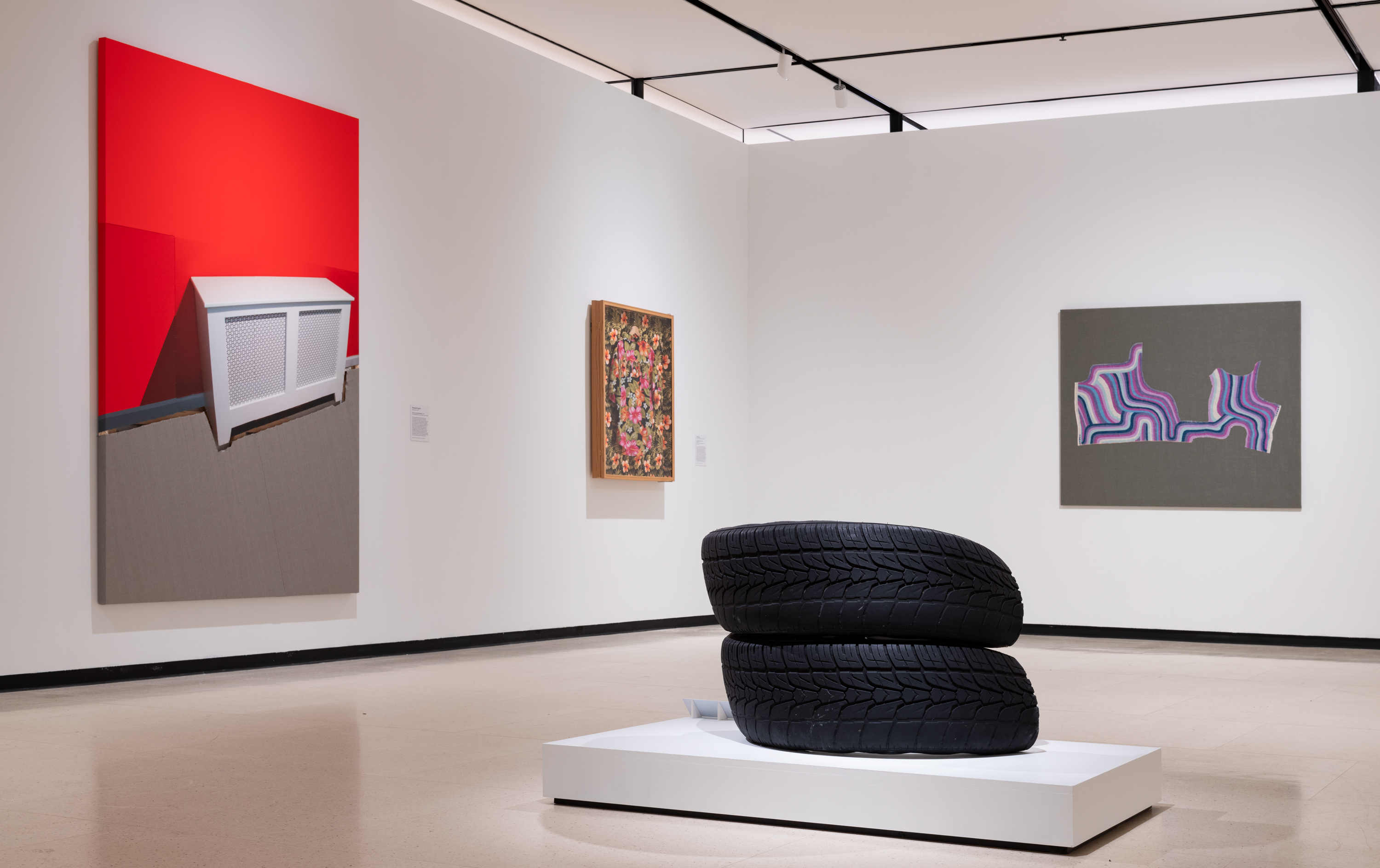 Installation view of a gallery with three works hanging on white walls and a sculpture made from a tire in the center of the space