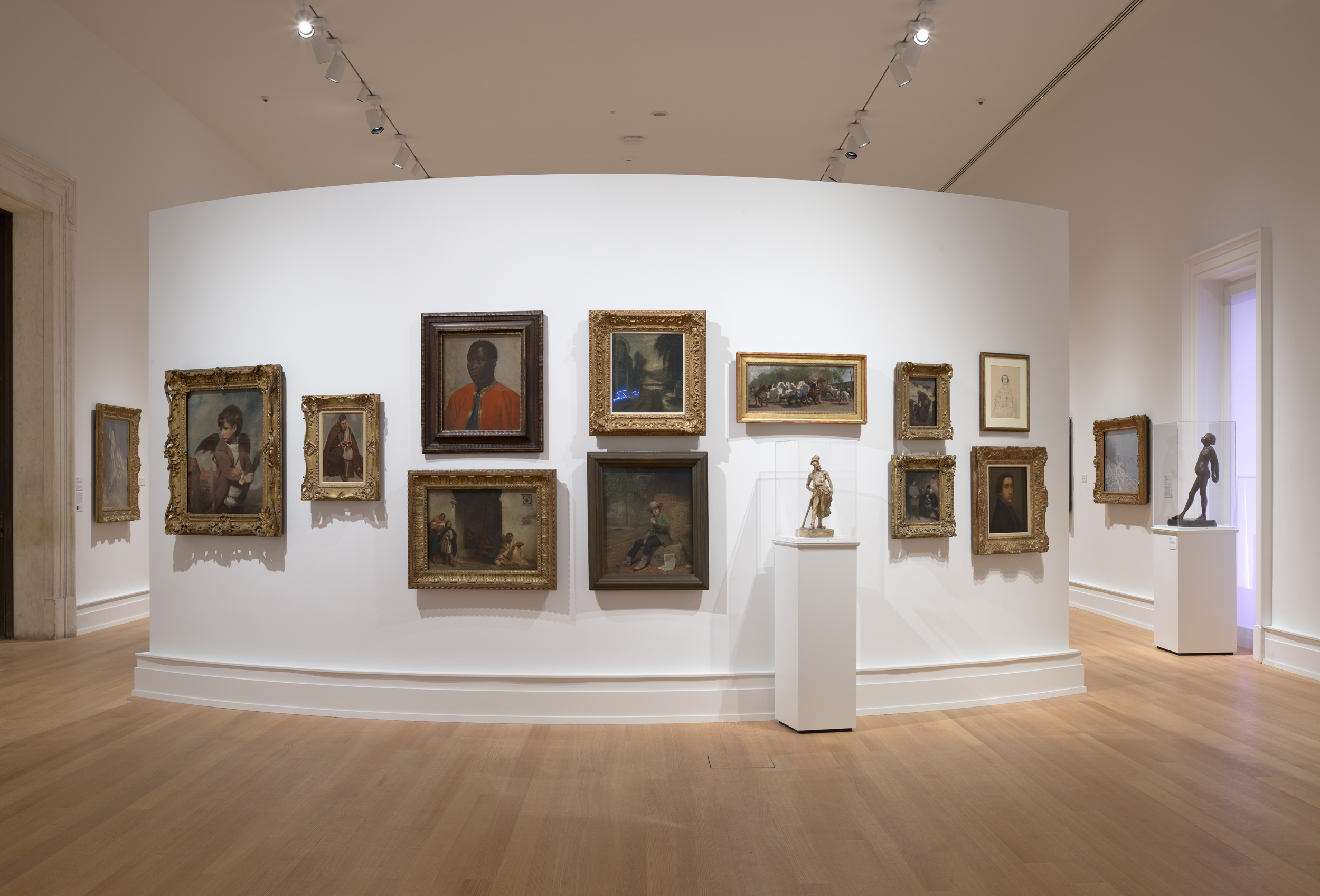 A salon-styled wall of paintings on a curved white gallery wall