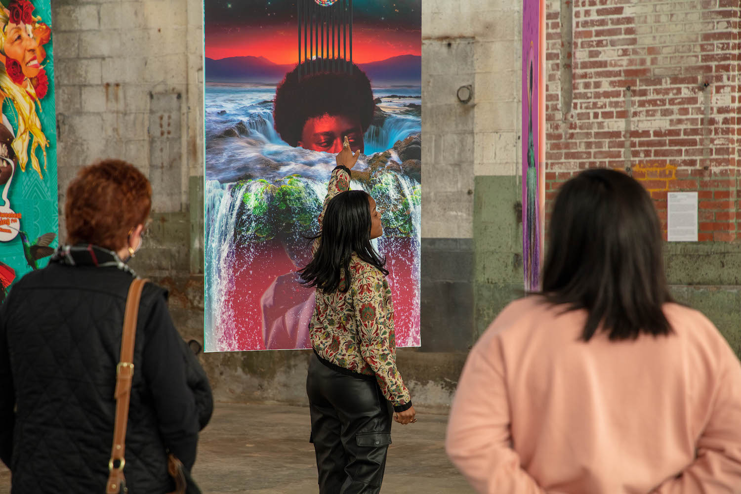 A woman of dark skin tone stands in front of an artwork