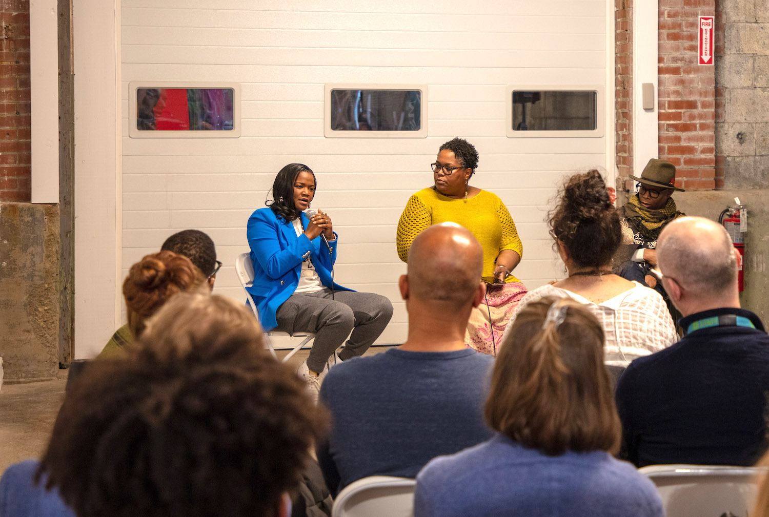 A woman of dark skin tone speaks on a panel in front of a crowd