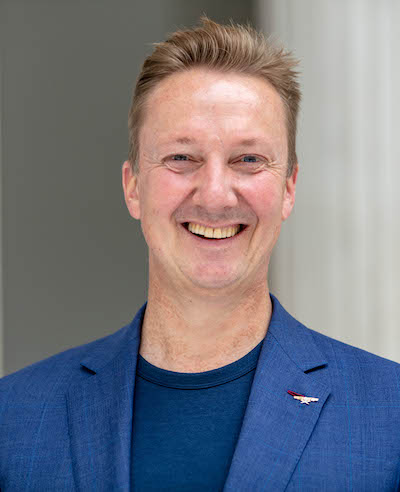 A headshot of a white man in front of a colorful painting