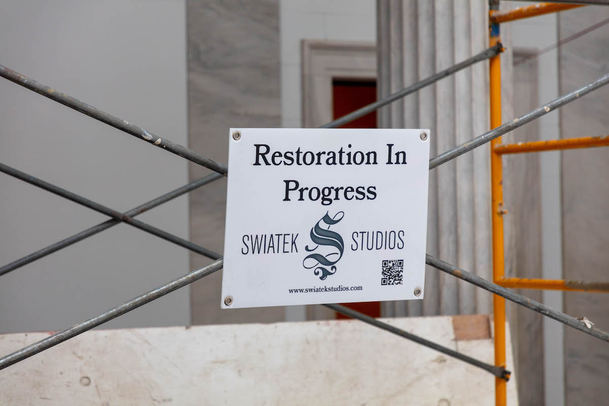 Sign that reads, "Swiatek Studios: Restoration in Progress" hung on an orange scaffold
