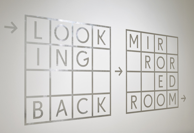 Silver vinyl installation saying "Looking Back: Lucas Samaras's Mirrored Room" 