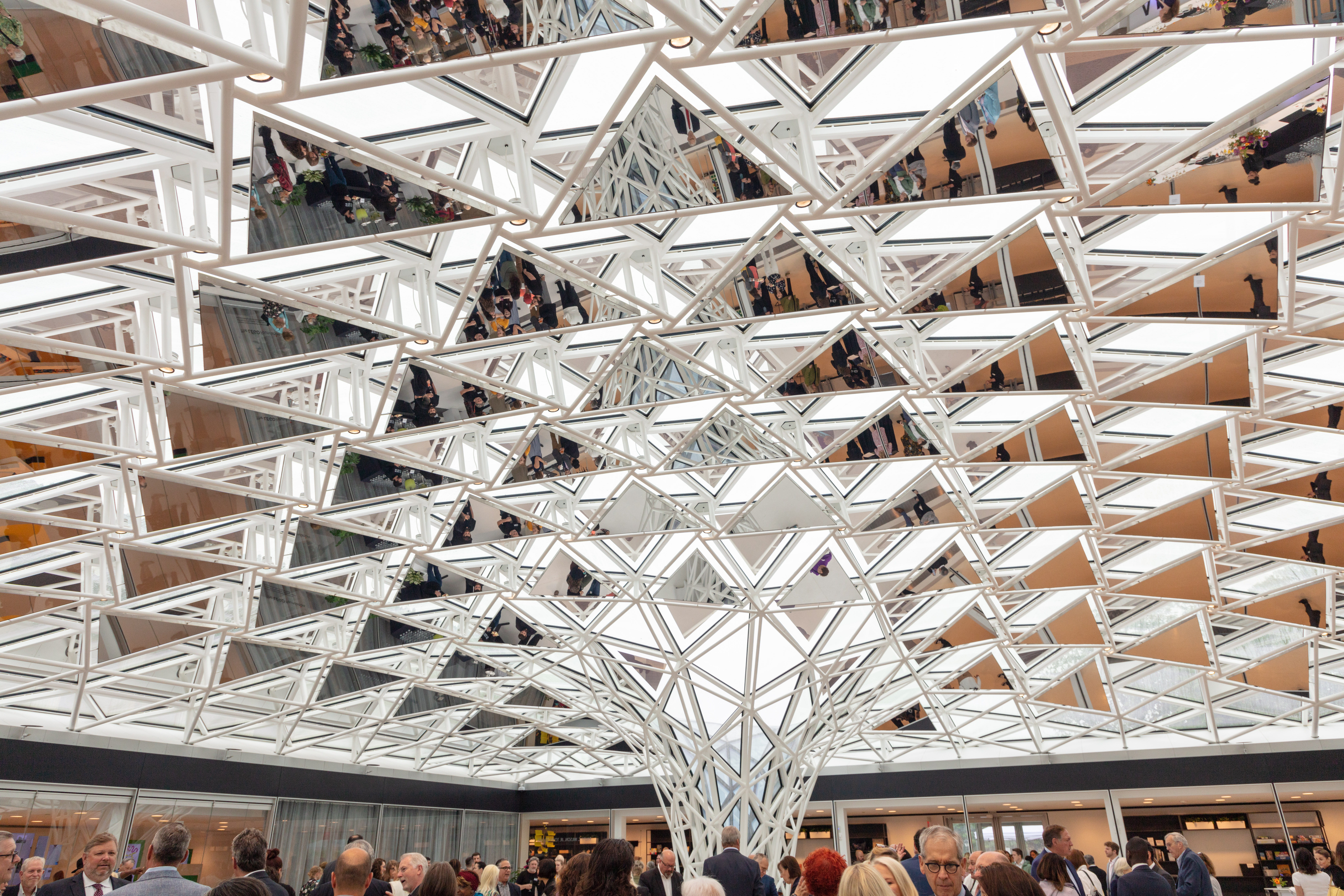 A mirrored, kaleidoscopic dome-like canopy over a courtyard full of people