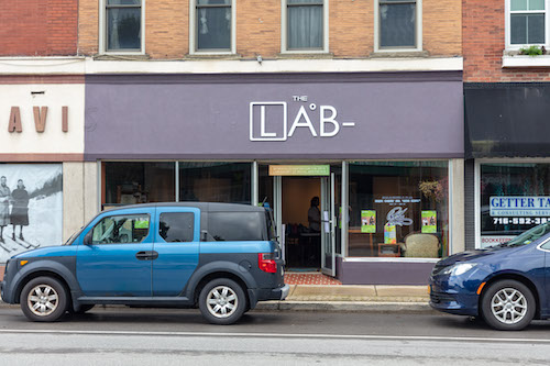 Two blue cars parked in front of a brick storefront with a sign that says LAB