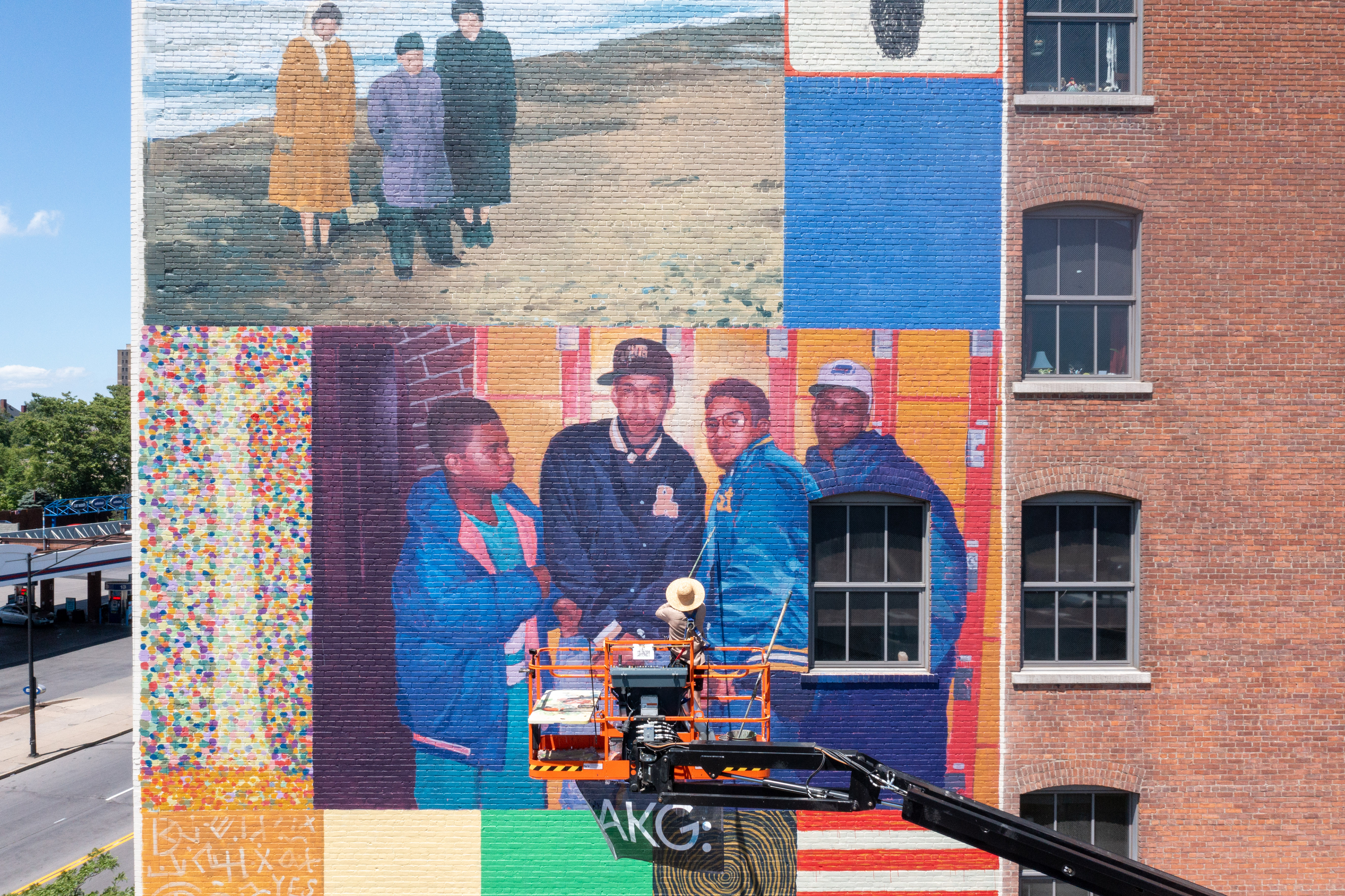 Drone view of an artist on a lift working on a large mural on the side of a building