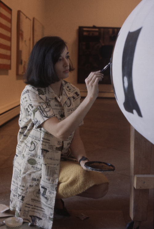 A woman with short dark hair kneeling down and painting a sculpture
