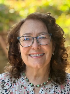 A person with long dark hair and light skin tone wearing glasses and smiling