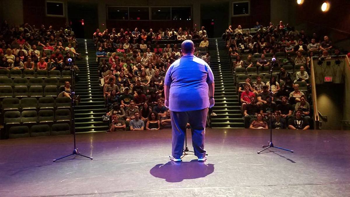 Burton stands before a crowd, back to the camera, bathed in purple light