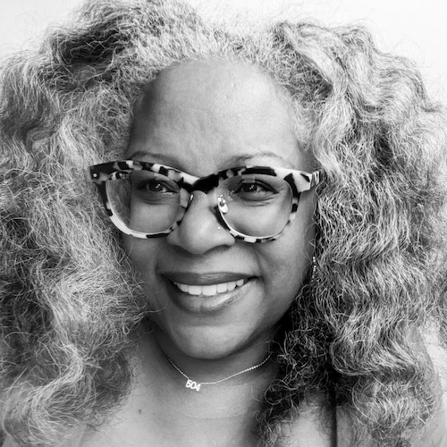 Black and white image of a woman with curly hair, medium to dark skin tone, and marbled glasses
