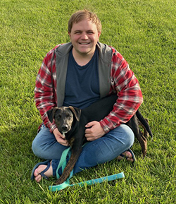 Photo of Cody Mejeur sitting on green grass holding a dog