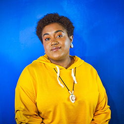 An African American woman in a yellow sweatshirt in front of a blue background