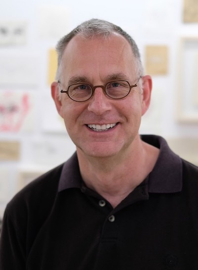 A man of light skin tone with gray hair and glasses smiling