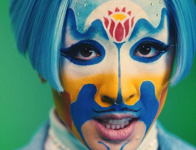 A closeup of a person in blue and yellow facepaint and a blue wig