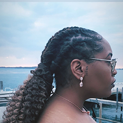 Profile of a Black woman wearing sunglasses with long hair in braids and a ponytail