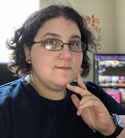 Photo of Joan Nobile, with brown curly hair and glasses, holding her hand to her face