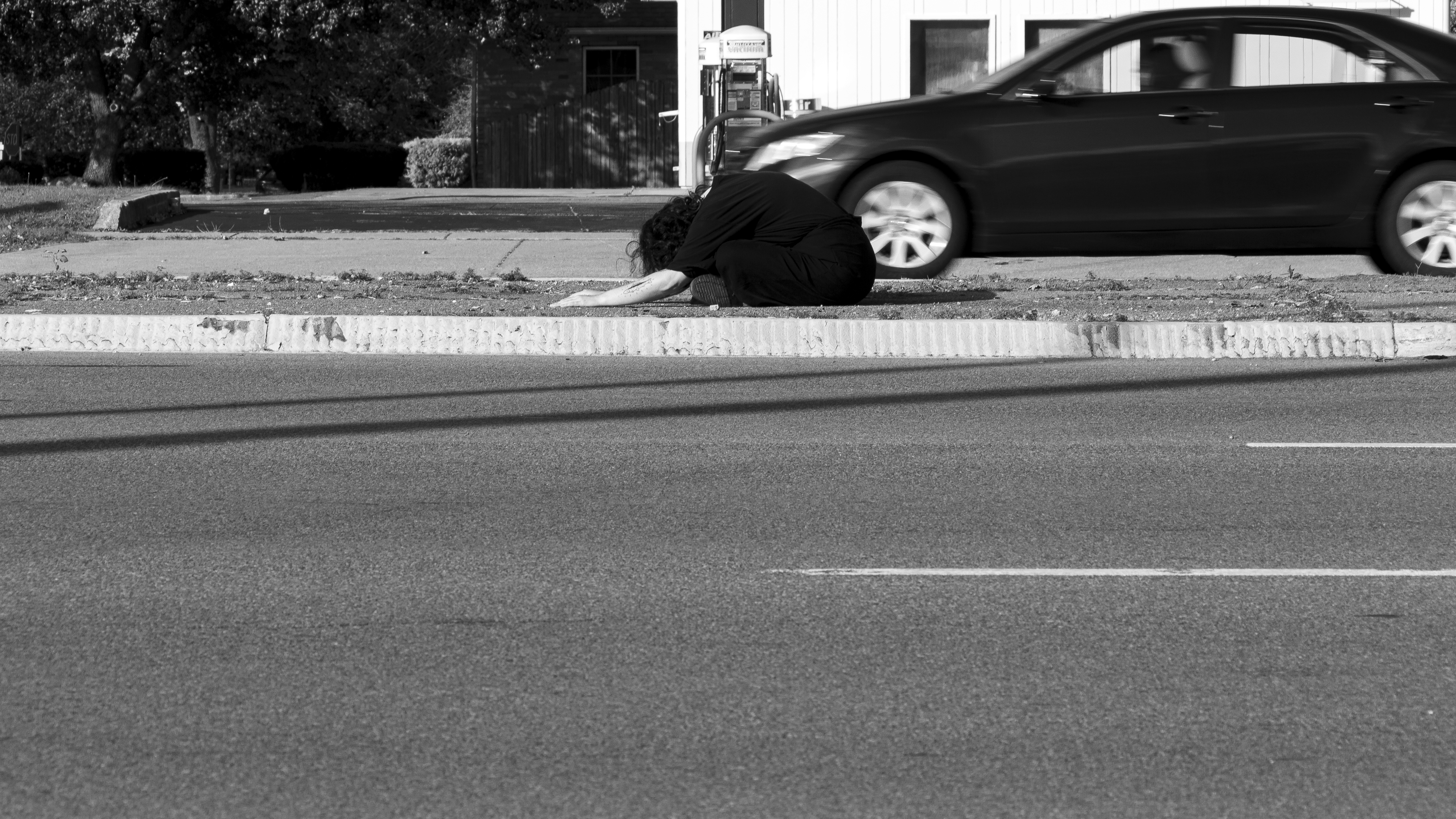 Black and white still image of a person bowing on the ground of a median