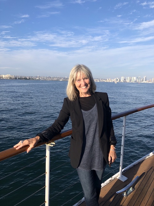 A woman with grey hair leaning on the rail of a boat out on the water