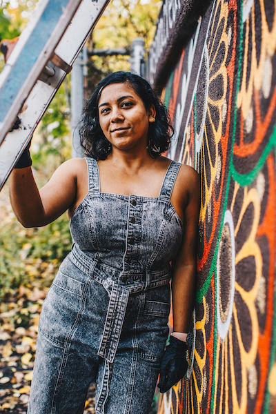 A woman leaning against a mural on an outdoor wall, holding onto a ladder