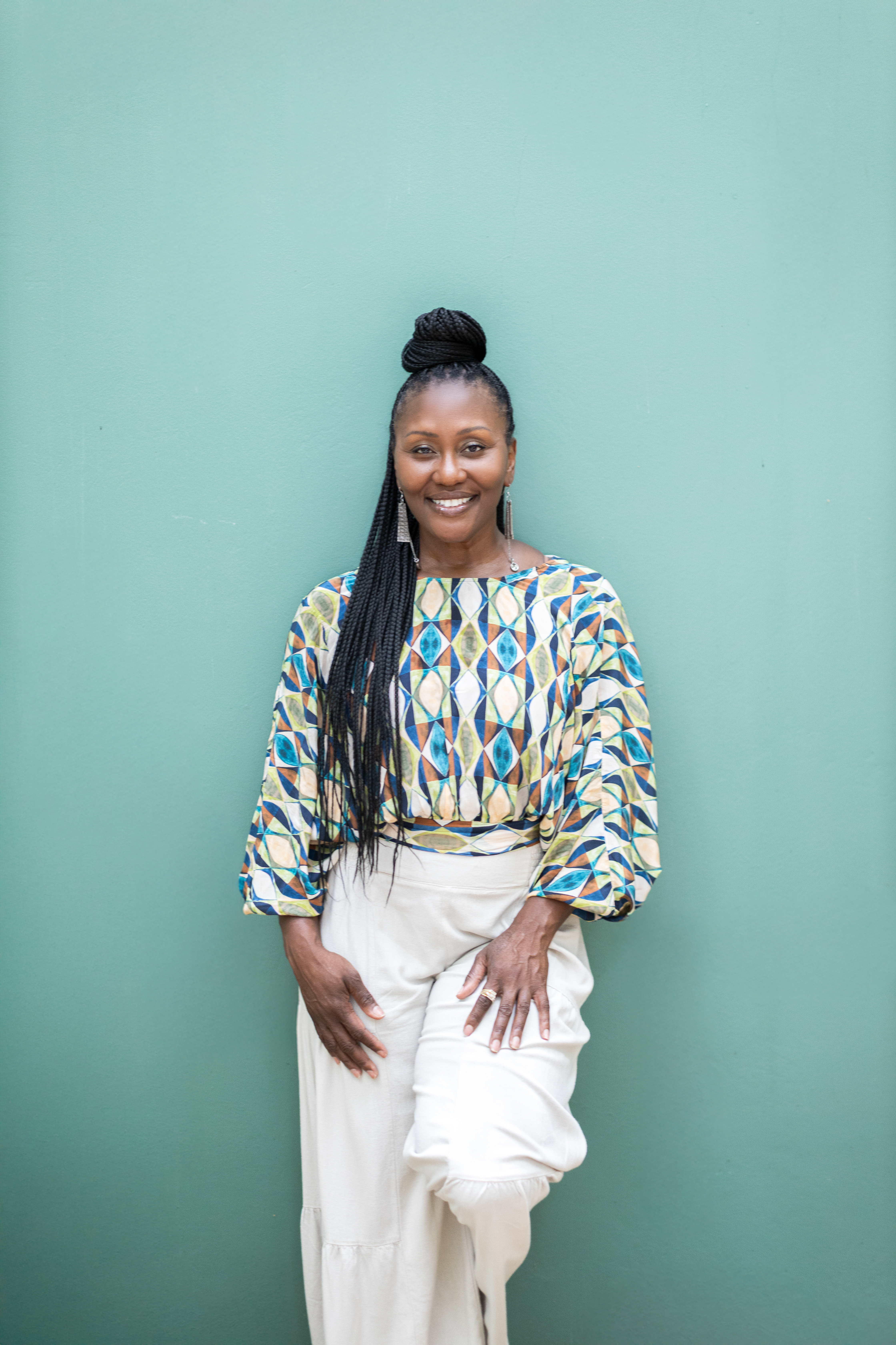A person in a patterned shirt and white pants in front of a green background
