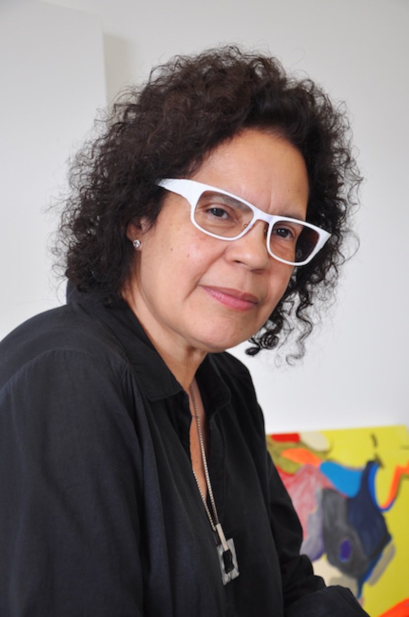 Headshot of a person with dark curly hair, wearing white glasses