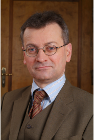 Headshot of a man with light skin tone, glasses, and wearing a brown suit