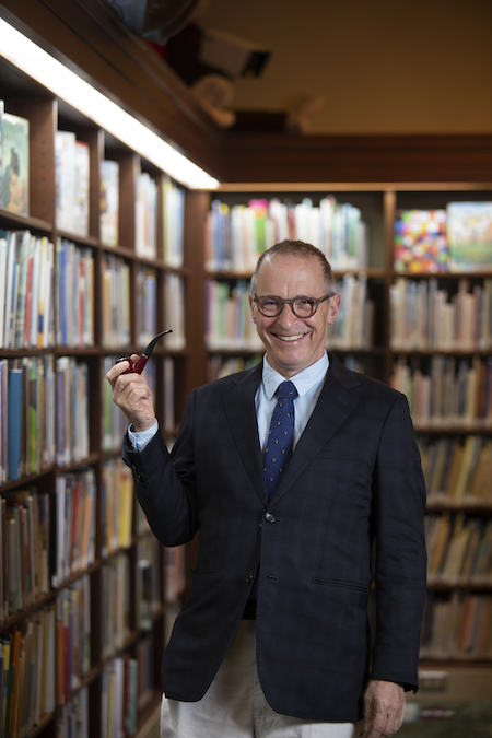 Photo of David Sedaris in a suit in a library holding a pipe