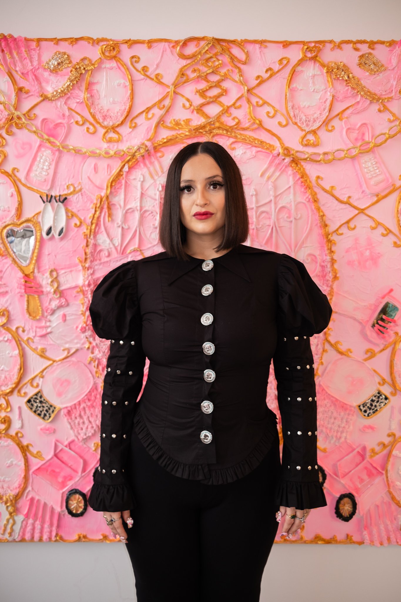 A person in a black dress, standing in front of a pink background