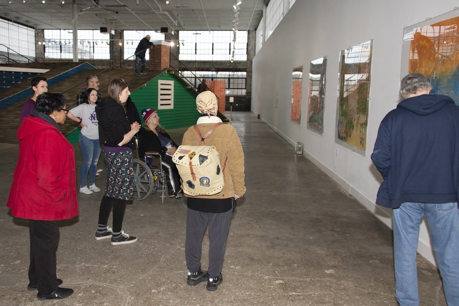 A group of adults, including one in a wheelchair, looks at a series of paintings