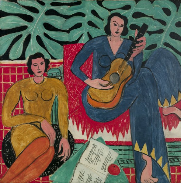 Two women look out toward the viewer from this brightly colored painting. The artist depicted these women using simple, flat shapes with dark outlines. The woman in a caramel colored dress at left sits on a floor cushion next to sheet music. The woman at right wears a marine blue jumpsuit with yellow triangles at the bottom of the legs. She has one foot on the floor and one on the couch on which she sits while playing guitar. A red tile floor contrasts with a black wall decorated with large green leaves.
