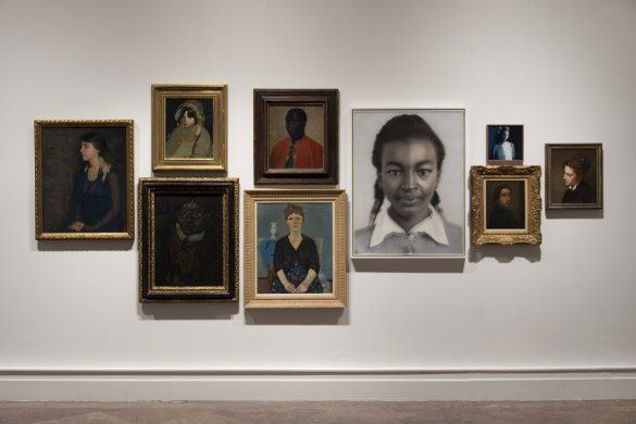 A photograph of nine photographs and paintings hung on a white wall