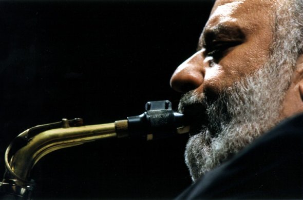 A close up photograph of a man blowing into a saxophone