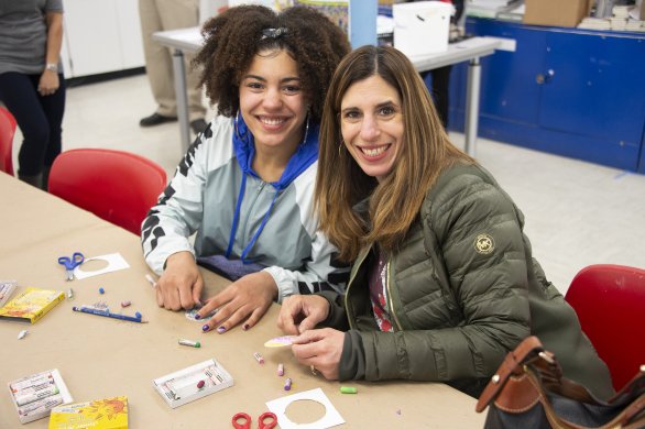 Two women smiling at the camera while doing an art activity in the classroom