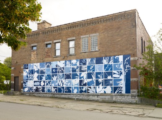 A large mural on an exterior wall of a brick building that is made up of rectangles of blue and white plant shapes