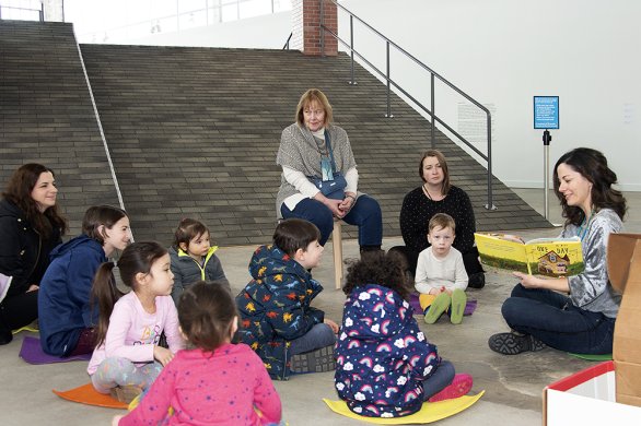 A group of children sitting on the floor listening to an adult read a book