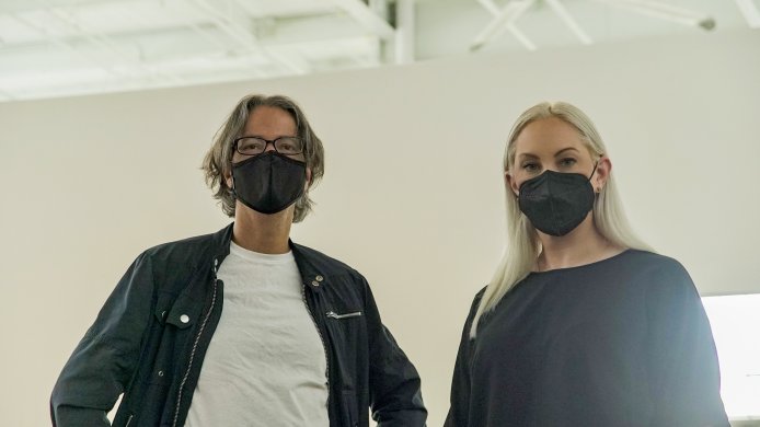 A man and a woman wearing face masks with a white wall in the background