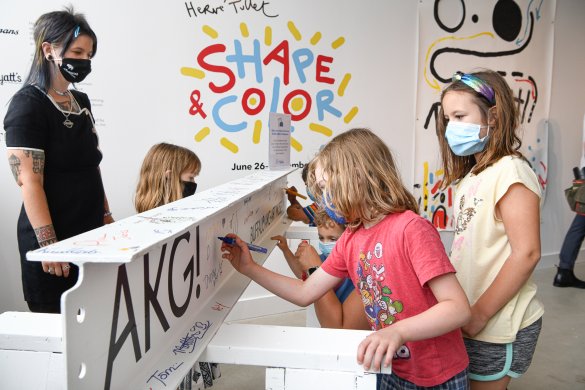 A woman and three kids sign their names on a steel beam painted white with the new Buffalo AKG Art Museum logo on it in black letters