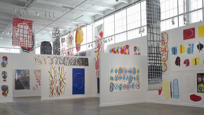 Installation view of colorful works on white walls in an industrial building