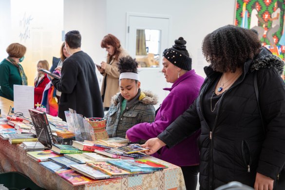 A diverse group of people gather around a table with an array of books on it