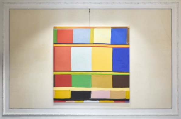 Photograph showing canvas of multi-colored, roughly circular shapes on top of a grid of differing colors hung on an ornate white wall