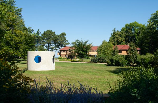 Image of concrete sculpture on a green, wooded pastoral landscape with red-roofed structure in the background