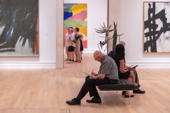 a man sitting on a bench writing in an art gallery