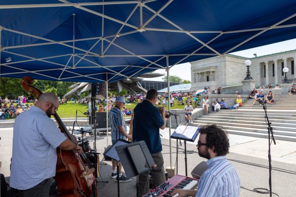 A Jazz band performing under a blue tent outdoors 