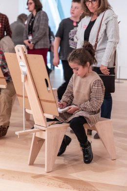 A young girl drawing on a wooden drawing horse in a gallery