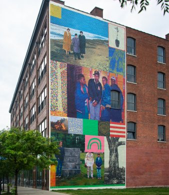 A large mural on a tall brick building in various bright colors with imagery of people throughout