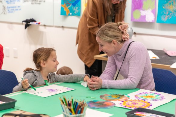 A mother and daughter smiling at each other while working on an art project